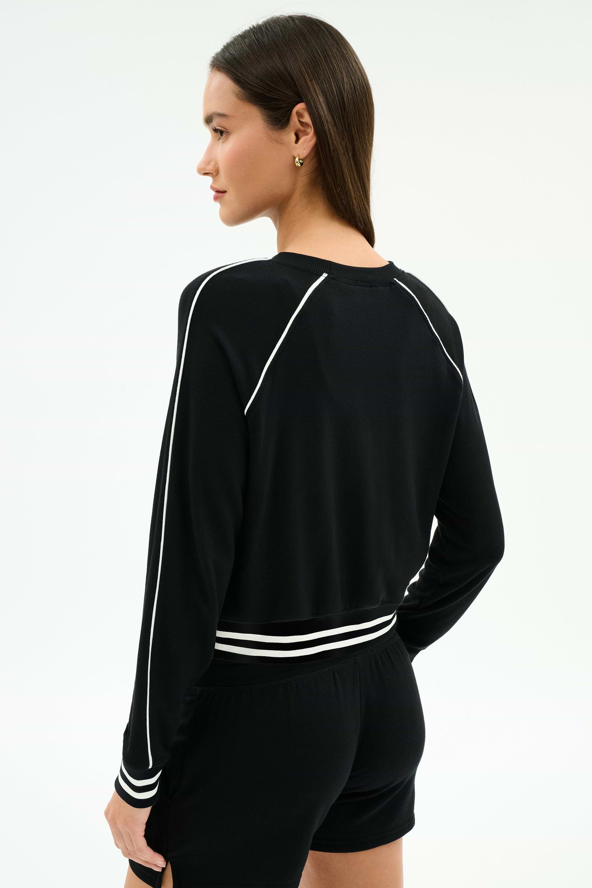 A person wearing the SPLITS59 Brooks Fleece Sweatshirt With Stripe in black/white, paired with matching black shorts, is seen from behind against a plain background.