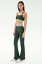 A woman stands against a plain background wearing the SPLITS59 Cali Active Rib Bra in Heather Military, paired with matching high-waisted flared leggings featuring white stripes and silver sneakers.