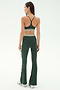 A woman faces away in the SPLITS59 Raquel Active Rib Flare - Heather Military set, featuring a dark green spandex sports bra and matching high-waisted flared leggings, paired with white sneakers against a plain light background.