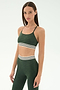 A woman wears the SPLITS59 Cali Active Rib Bra in Heather Military, featuring green spandex fabric and high-waisted leggings with white and black striped bands, standing against a plain light background.