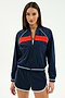 A woman faces forward wearing the SPLITS59 Carrie Woven Nylon Jacket in Indigo/Lotus Red, paired with matching navy blue spandex shorts featuring white trim.