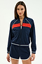 A woman faces forward wearing the SPLITS59 Carrie Woven Nylon Jacket in Indigo/Lotus Red, paired with matching navy blue spandex shorts featuring white trim.