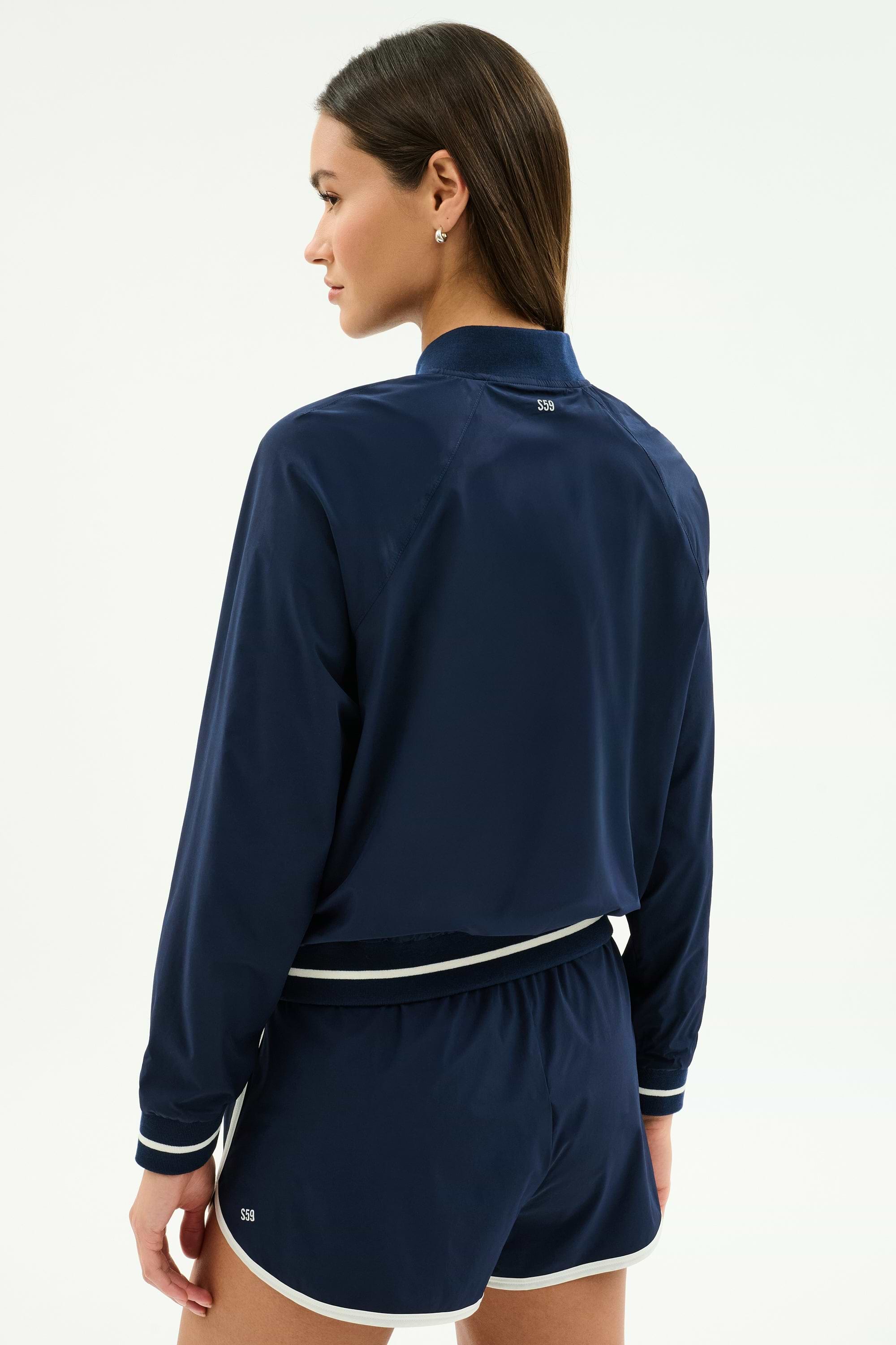 A person faces away, wearing the SPLITS59 Carrie Woven Nylon Jacket in Indigo/Lotus Red against a plain background.