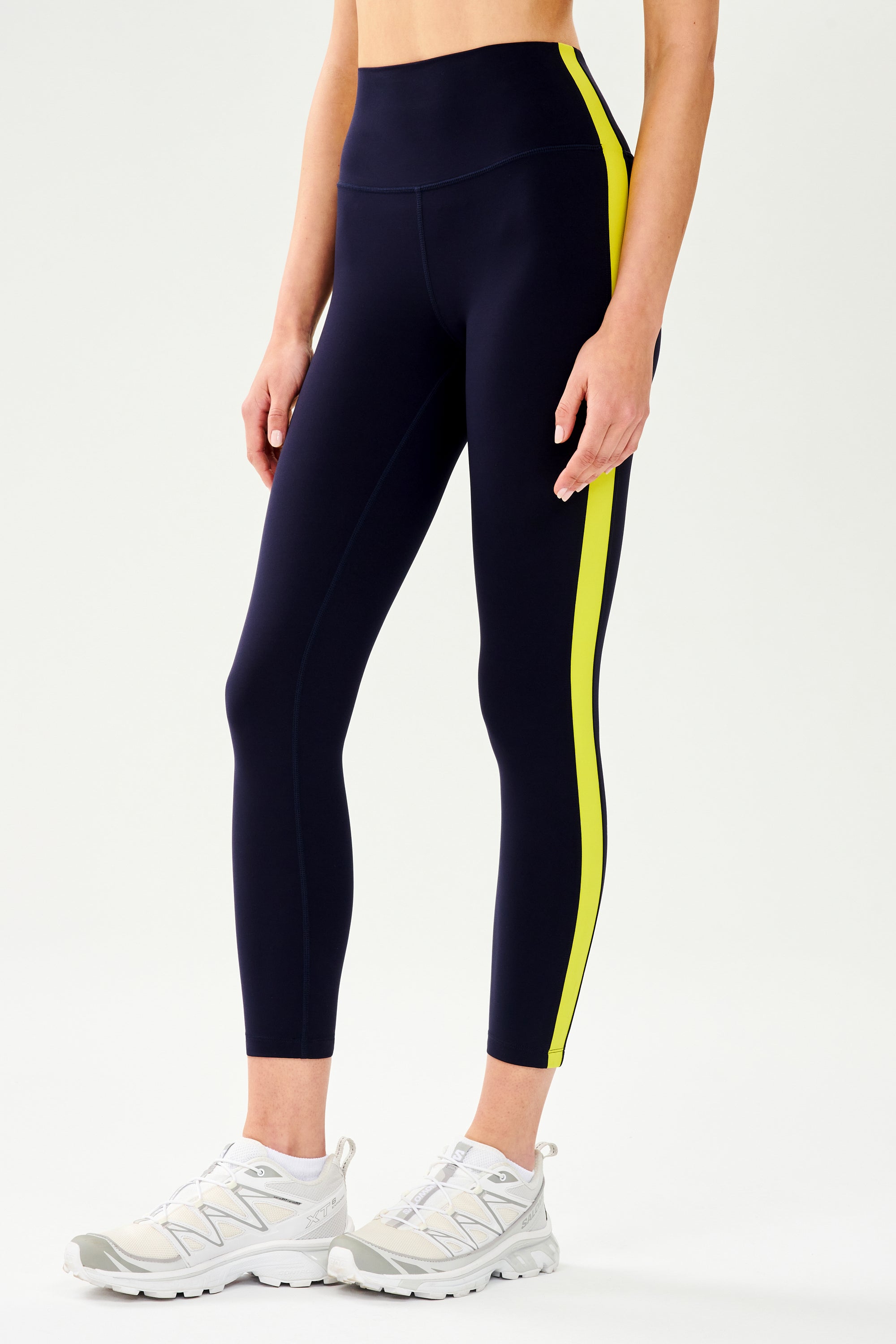 Side view of girl wearing dark blue leggings with a yellow down the side with white shoes