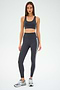 A person wearing a dark athletic outfit with an Ella Airweight Bra from SPLITS59 in Graphite/White and ultra luxe sneakers stands against a plain background, looking forward confidently.