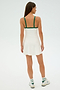 A woman models the SPLITS59 Monah Rigor Dress in White/Arugula, featuring breathable nylon and green straps, as she faces away against a light background. Her look is completed with sleek white sneakers and socks adorned with green stripes.