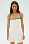 A woman stands against a plain background, wearing the Monah Rigor Dress - White/Arugula by SPLITS59. This sleeveless dress features green straps and elegantly hugs her form, crafted from a blend of spandex and nylon for a comfortable fit.