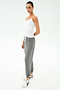 Person standing against a plain background, wearing the SPLITS59 Loren Seamless Waist Length Tank in white, gray drawstring sweatpants, and white sneakers with black accents.
