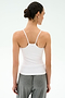 A person faces away, wearing the SPLITS59 Loren Seamless Waist Length Tank in white and gray pants, hair tied back in a low bun, set against a plain light background.