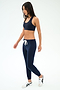 A woman wearing SPLITS59 Sonja Fleece Sweatpant in Indigo, styled with a navy sports bra and white sneakers, stands against a plain white background.