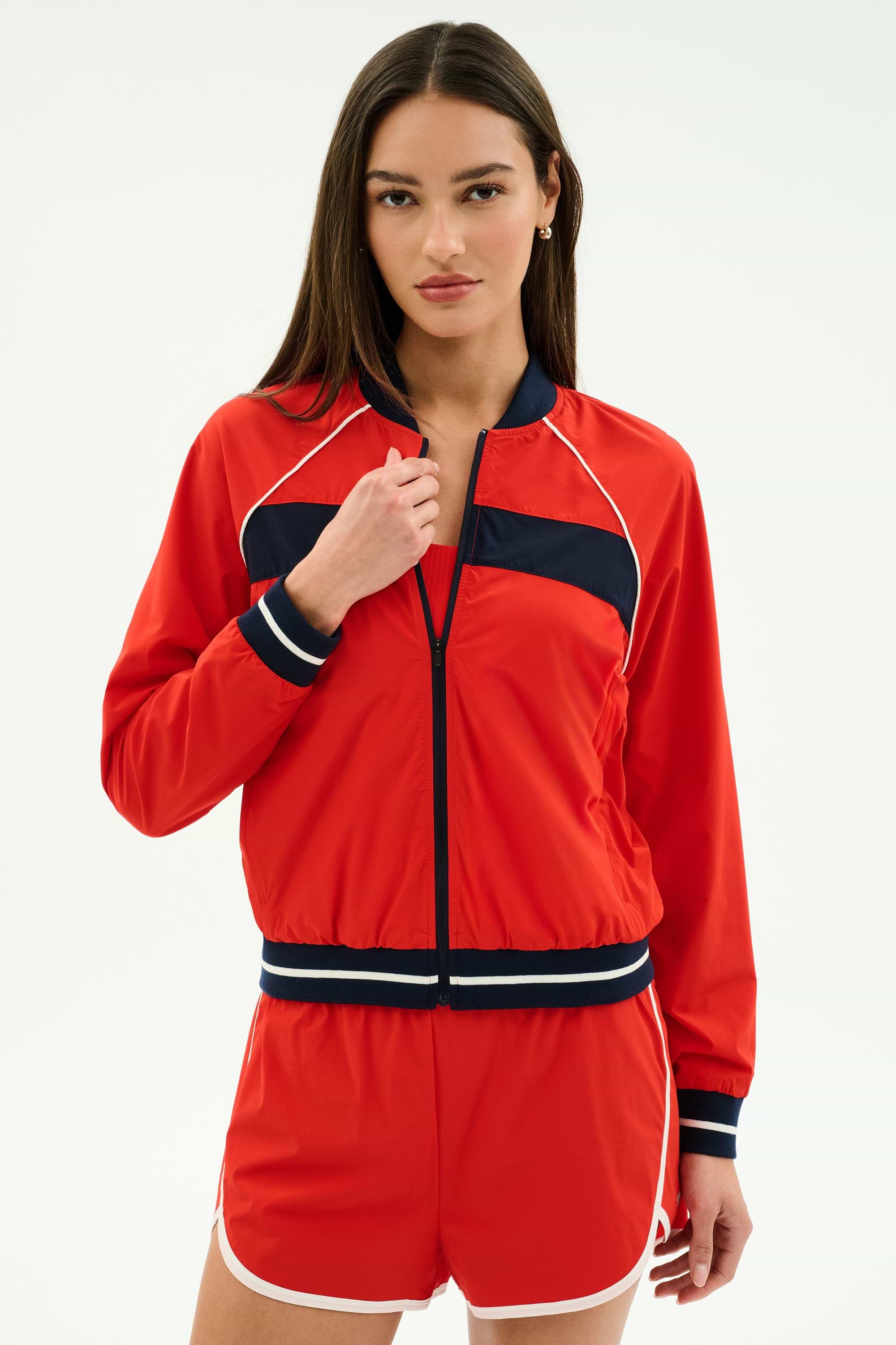 A woman poses against a plain light background wearing the SPLITS59 Carrie Woven Nylon Jacket in Lotus Red/Indigo, featuring navy and white accents and crafted from a comfortable nylon-spandex blend.