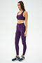 A woman in purple athletic wear, featuring a SPLITS59 Ella Airweight Bra in Black Currant/Indigo, and blue sneakers stands on a plain background, looking to the side.