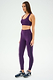 A woman in purple athletic wear, featuring a SPLITS59 Ella Airweight Bra in Black Currant/Indigo, and blue sneakers stands on a plain background, looking to the side.