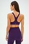 A person is wearing the Ella Airweight Bra in Black Currant/Indigo by SPLITS59, featuring a racer back, which is perfect for hot yoga. They pair it with matching leggings as they face away.