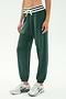 Model wears SPLITS59 Andie Oversized Fleece Sweatpant W/ Stripe - Military, featuring a soft spandex blend, white drawstring, and striped waistband, paired with white sneakers against a plain light background.