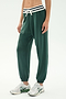 Model wears SPLITS59 Andie Oversized Fleece Sweatpant W/ Stripe - Military, featuring a soft spandex blend, white drawstring, and striped waistband, paired with white sneakers against a plain light background.