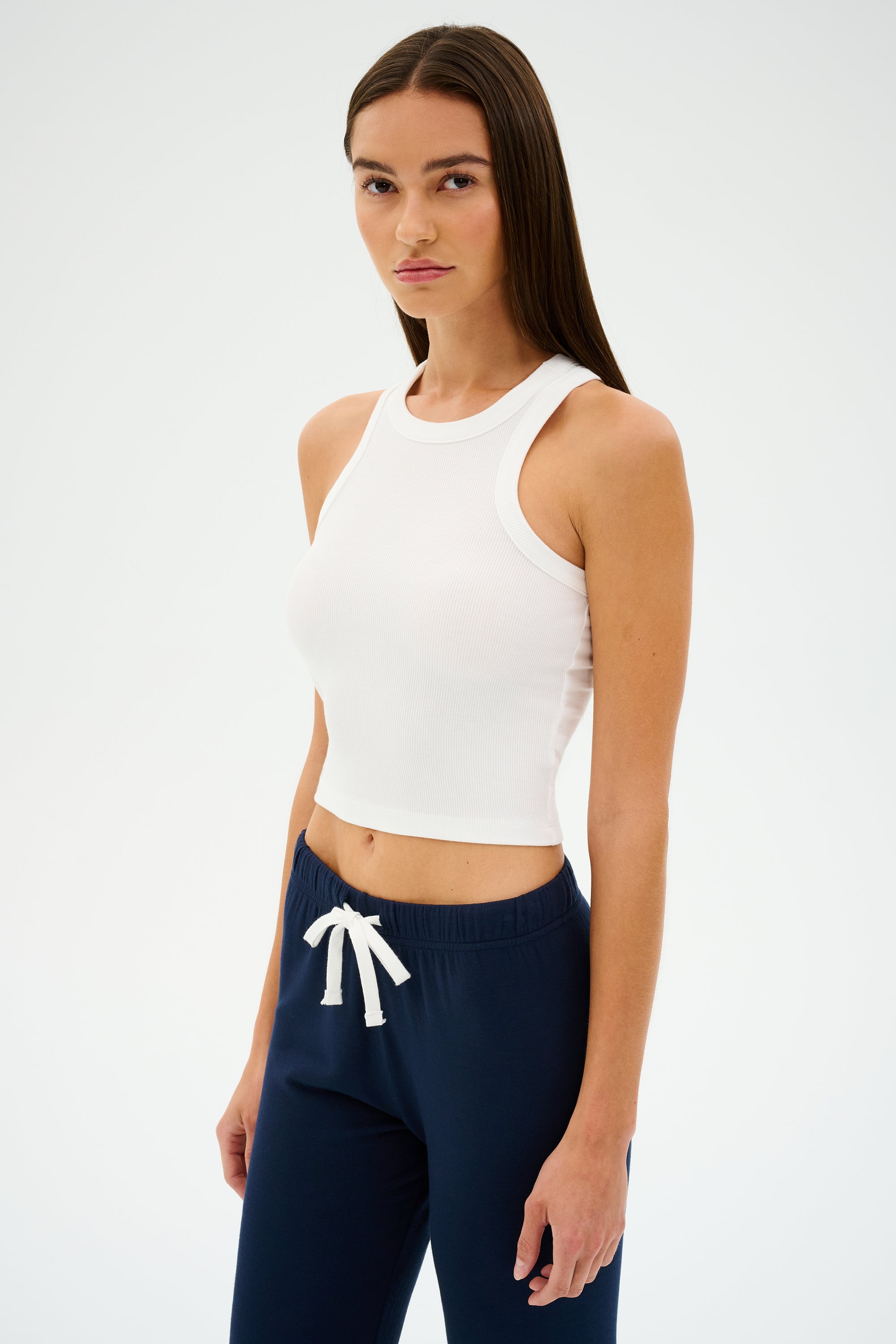 Someone in a SPLITS59 Kiki Rib Crop Tank - White and dark drawstring pants stands against a plain background.