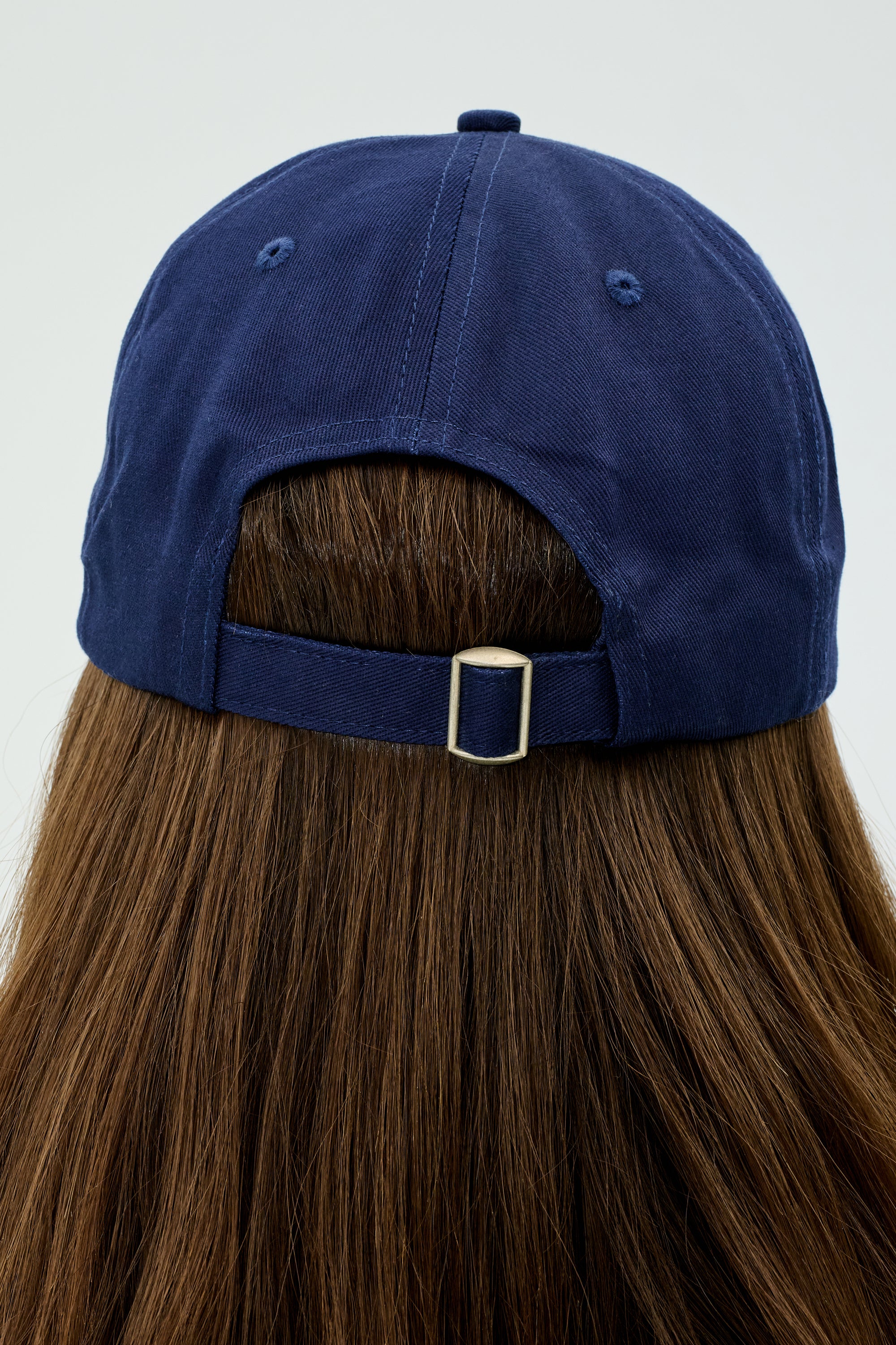 A person is seen from the back wearing a Tennis Cap - Indigo by SPLITS59, with long brown hair flowing beneath it.