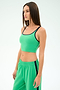 A woman with straight brown hair wears the SPLITS59 Cait Rigor Bralette in Grass/Indigo with matching green pants featuring a black stripe, standing against a plain light background.
