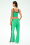 A woman faces away, wearing the SPLITS59 Cait Rigor Bralette in Grass/Indigo with matching green track pants featuring black stripes and white sneakers, set against a light background.