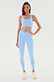A person stands against a white background wearing a SPLITS59 Sprint Rigor Bra in Skylight and matching leggings, paired with white sneakers, perfect for gym workouts.