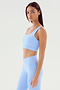 A woman stands facing slightly to the right, wearing a light blue Sprint Rigor Bra - Skylight and matching leggings from SPLITS59, designed with ultra luxe Rigor fabric for superior multi-sport performance.