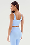 A woman with long hair stands sideways, wearing a light blue Sprint Rigor Bra - Skylight from SPLITS59 and matching high-waisted leggings, perfect for gym workouts.