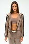 A woman with straight brown hair wears the SPLITS59 Reggie Water Repellent Jacket in Latte/Black, styled with matching taupe sportswear, against a plain white background.