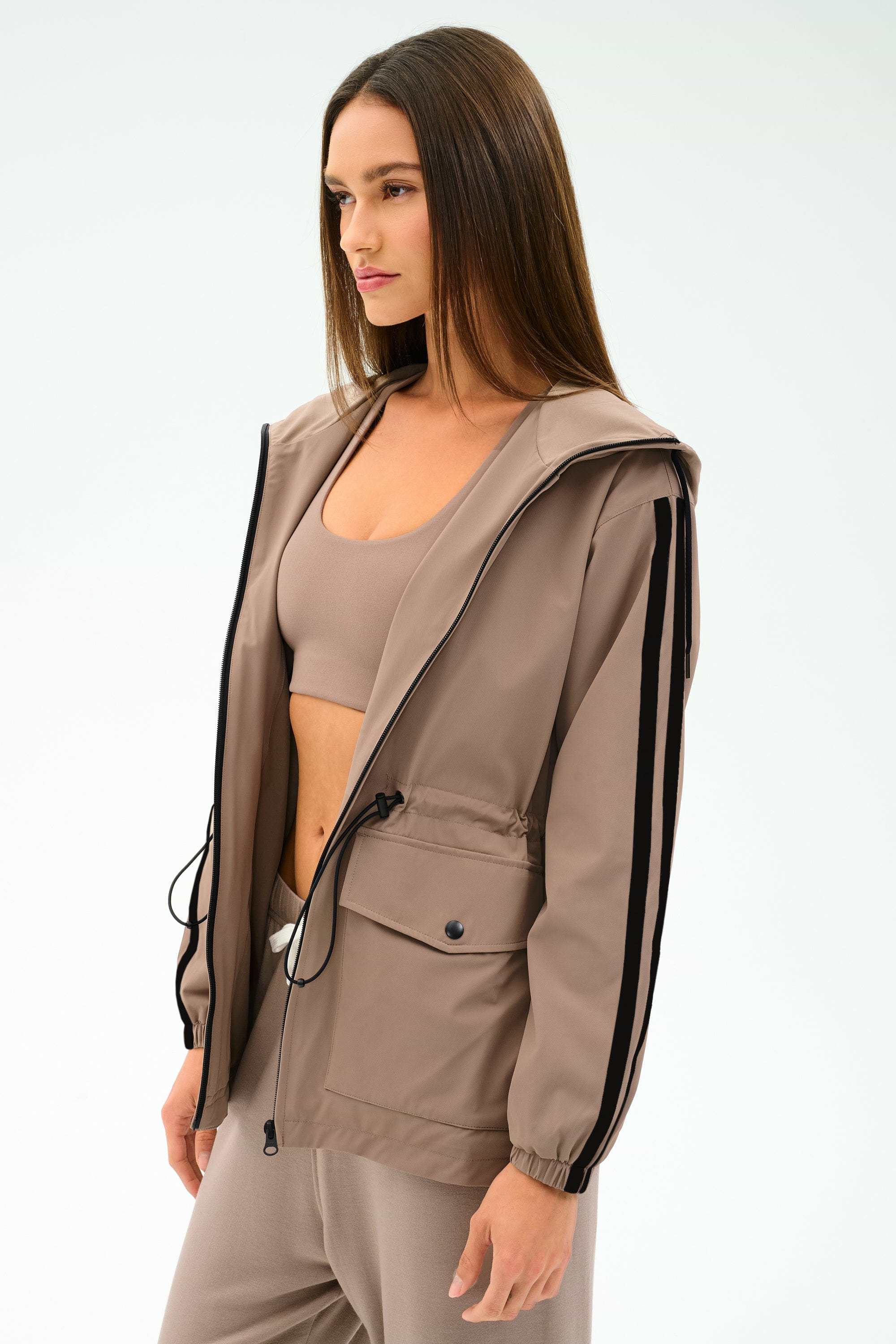 A woman models the SPLITS59 Reggie Water Repellent Jacket in Latte/Black over matching activewear, standing against a plain background.