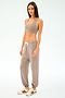 A woman stands against a plain background in a taupe sports bra, SPLITS59 Andie Oversized Fleece Sweatpant - Latte with white drawstring, and white sneakers with brown stripes—ideal for cool weather workouts or warm-ups.