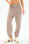 Wearing SPLITS59's Andie Oversized Fleece Sweatpant in Latte, featuring a drawstring waist and cuffed ankles, paired with white sneakers with maroon stripes—ideal for cool weather workouts or warm-ups against a plain background.