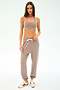 A woman stands against a plain background wearing a beige sports bra, SPLITS59 Andie Oversized Fleece Sweatpant in Latte with a drawstring, and white sneakers with maroon stripes—ideal for warm-ups or cool weather workouts.
