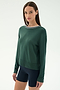 A woman with straight brown hair wears the SPLITS59 Sonja Fleece Sweatshirt W/ Stripe in Military and navy spandex bicycle shorts, standing against a plain light background.