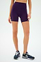 A person confidently poses in SPLITS59's Ella High Waist Airweight Shorts in Black Currant/Indigo, paired with navy running shoes against a pristine white background, ideal for conquering hot yoga sessions.