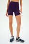 A person confidently poses in SPLITS59's Ella High Waist Airweight Shorts in Black Currant/Indigo, paired with navy running shoes against a pristine white background, ideal for conquering hot yoga sessions.