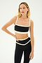 Dressed in stylish black and creme workout apparel, featuring the SPLITS59 Monah Rigor Bra, a person stands confidently with one hand on their hip against a simple background.