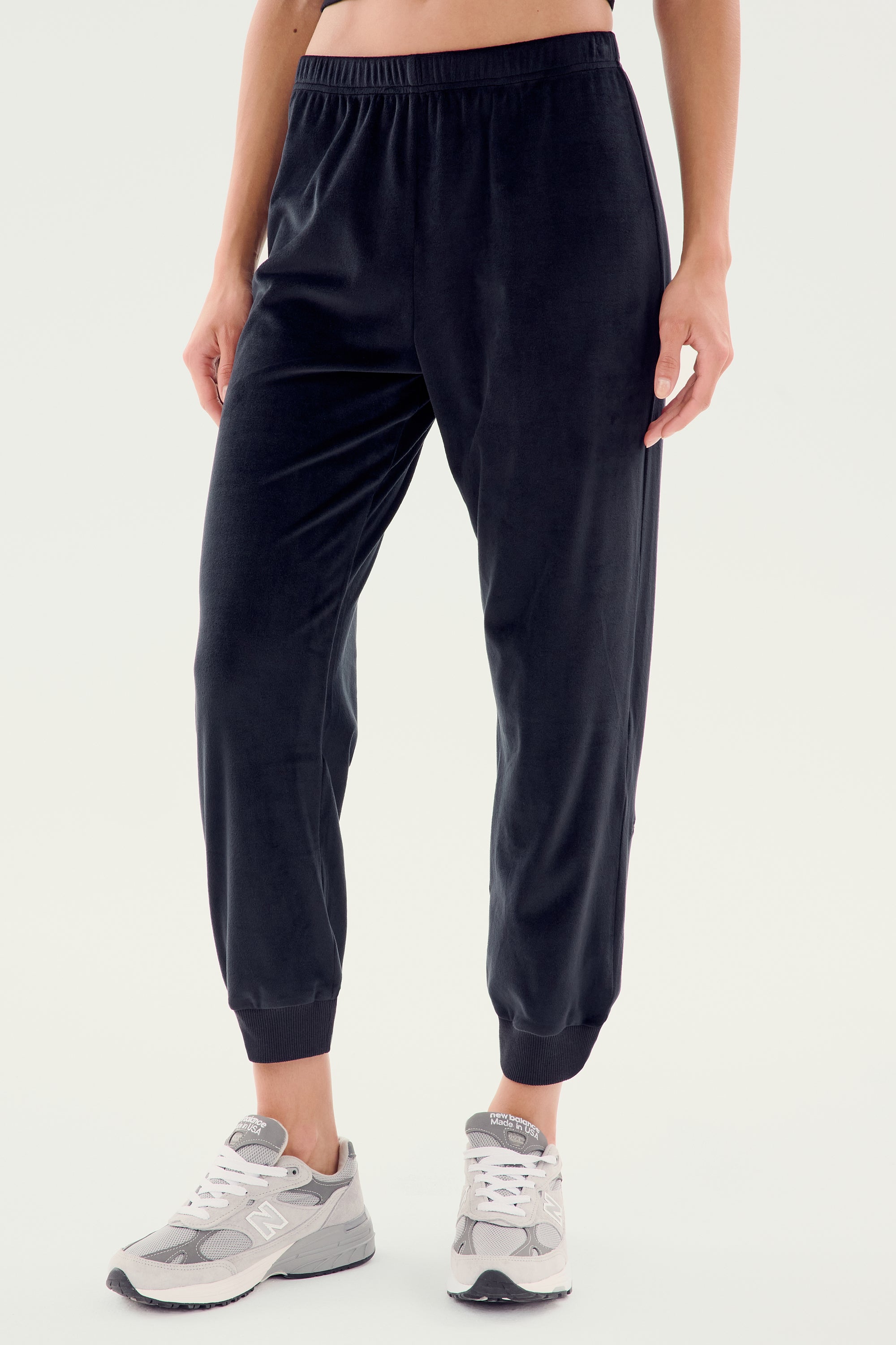 Person wearing black SPLITS59 Rhys Velour Jogger pants and gray sneakers, standing against a plain light background. Upper body is not visible, exemplifying effortless casual wear and ultimate comfort.