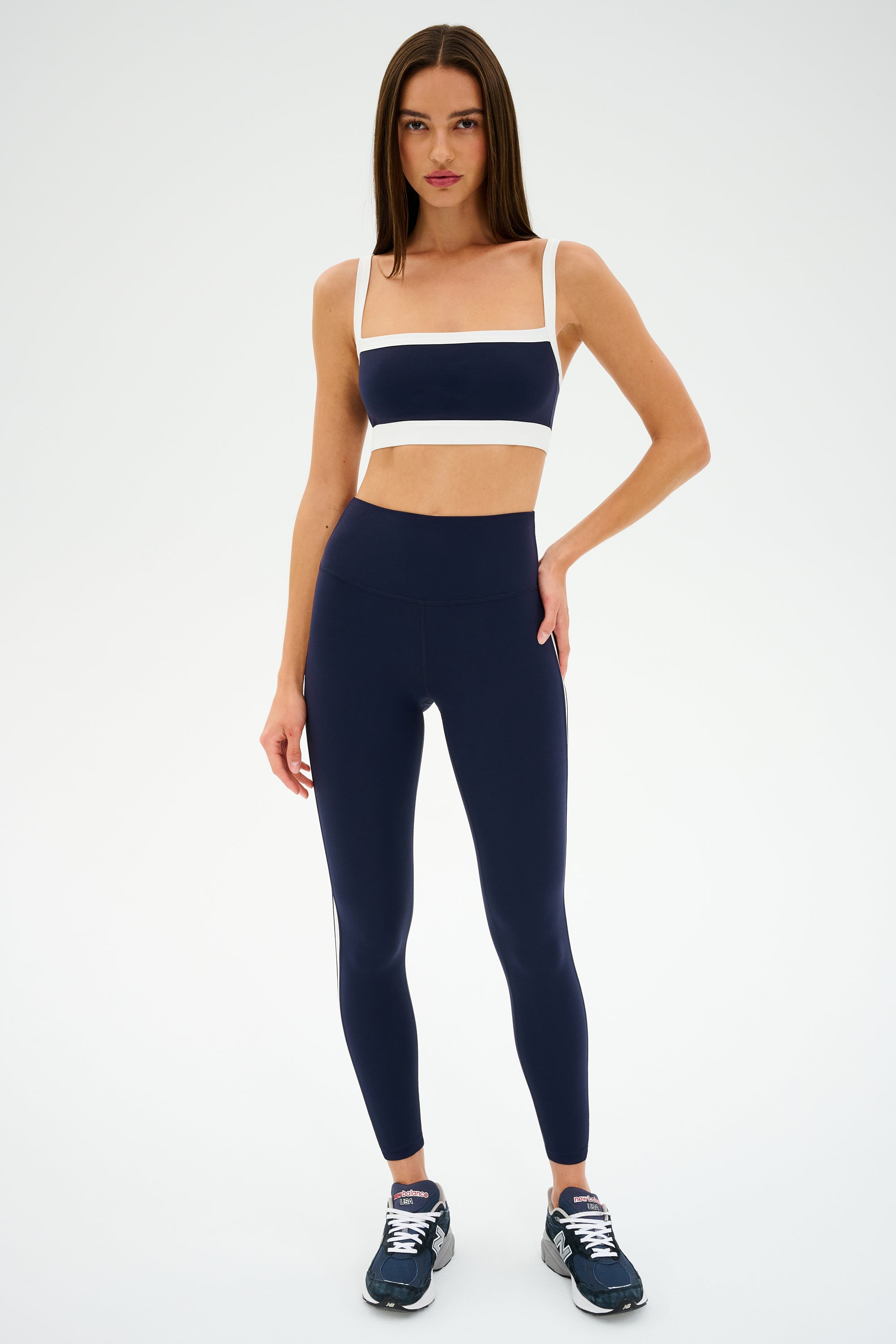 A person models confidently in a SPLITS59 Monah Rigor Bra - Indigo/White against a plain backdrop, hand on hip in chic sneakers. This outfit, ideal for gym workouts, merges comfort with performance effectively.