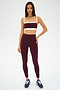 A woman stands against a plain background wearing the SPLITS59 Clare High Waist Rigor 7/8 leggings in Dark Cherry/Creme, paired with a matching sports bra, both crafted from a soft nylon-spandex blend and blue sneakers.
