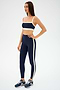 A woman wears the SPLITS59 Monah Rigor Bra in Indigo/Creme with matching leggings and navy running shoes, standing against a plain white background.