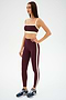 A woman stands against a plain white background wearing the SPLITS59 Monah Rigor Bra in Dark Cherry/Creme, paired with matching leggings and navy sneakers.
