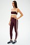 A woman stands against a plain white background wearing the SPLITS59 Monah Rigor Bra in Dark Cherry/Creme, paired with matching leggings and navy sneakers.