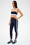 A person in the indigo and white SPLITS59 Monah Rigor Bra and athletic wear with sneakers stands against a neutral background, ready for their gym workout.