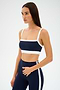 Against a plain background, a person in a blue and white athletic outfit exudes retro sport vibes. The Monah Rigor Bra by SPLITS59 combines solid support with style and function.