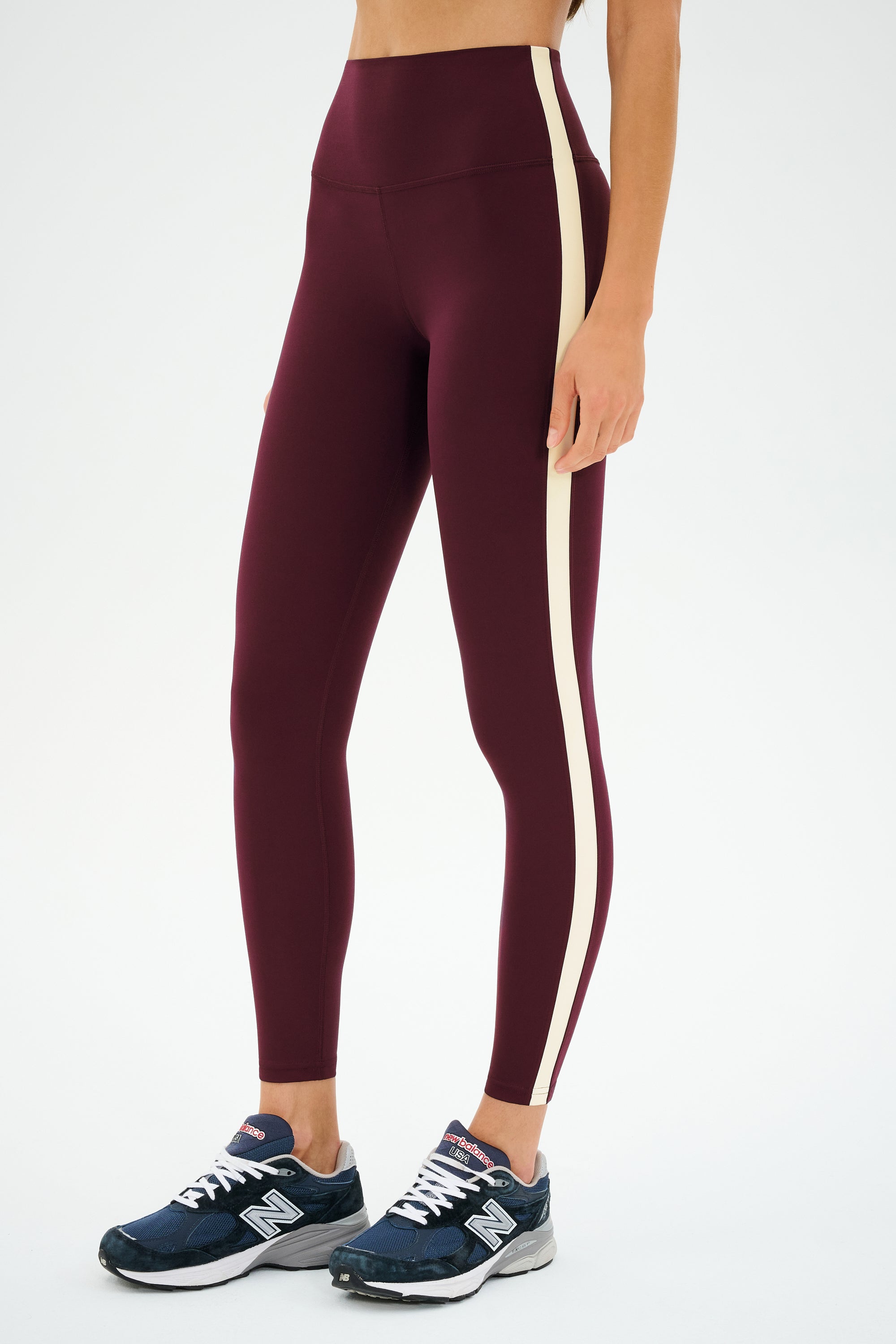 A person wearing SPLITS59 Clare High Waist Rigor 7/8 leggings in Dark Cherry/Creme and navy blue athletic shoes, standing against a plain white background.