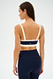 A woman faces away, wearing the SPLITS59 Monah Rigor Bra in Indigo/Creme with matching high-waisted leggings against a plain background.