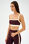 A woman models the SPLITS59 Monah Rigor Bra in Dark Cherry/Creme, a soft nylon-spandex workout set, standing against a plain white background and glancing to the side.