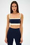 A woman with straight brown hair wears the SPLITS59 Monah Rigor Bra in Indigo/Creme, standing against a plain white background.