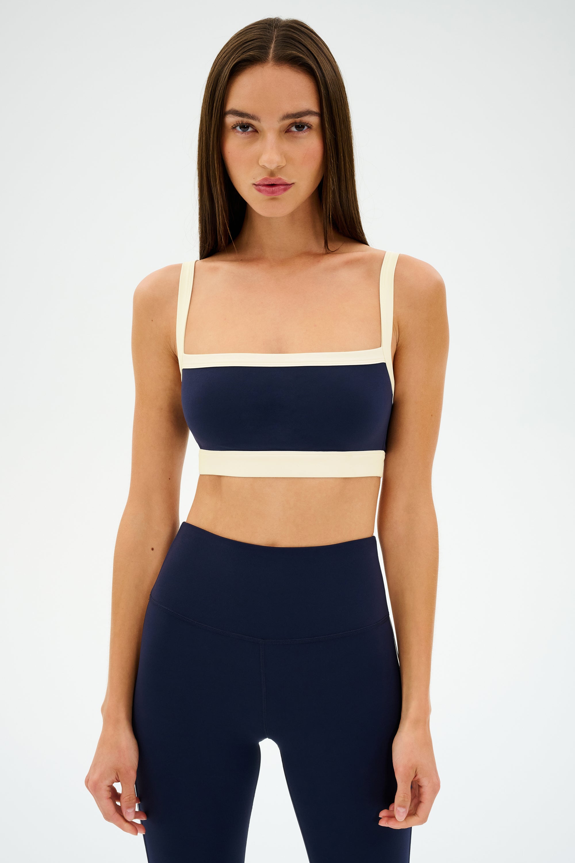 A woman with straight brown hair wears the SPLITS59 Monah Rigor Bra in Indigo/Creme, standing against a plain white background.