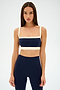 A woman with straight brown hair wears the SPLITS59 Monah Rigor Bra in Indigo/Creme, standing against a plain white background.